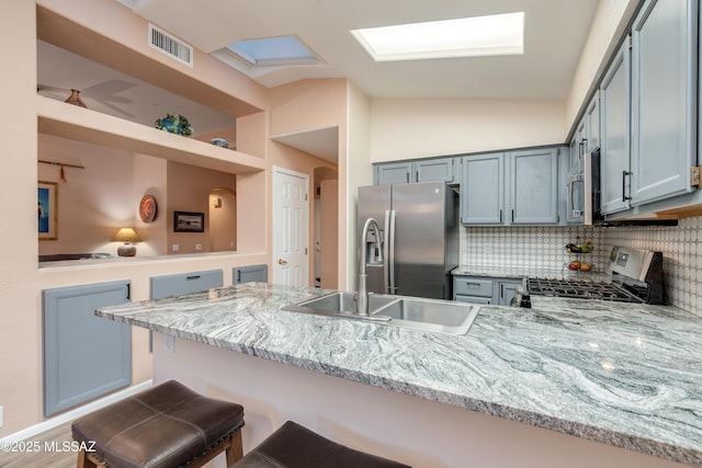 kitchen featuring a peninsula, light stone countertops, visible vents, lofted ceiling with skylight, and stainless steel appliances