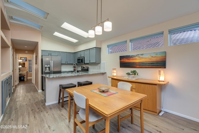 dining space with light wood-type flooring, baseboards, and lofted ceiling with skylight