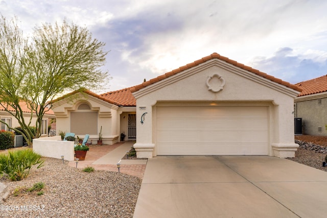 mediterranean / spanish-style home with cooling unit, stucco siding, a tile roof, an attached garage, and driveway