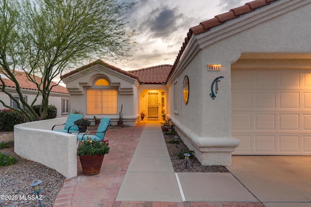 entrance to property with a tiled roof, an attached garage, and stucco siding