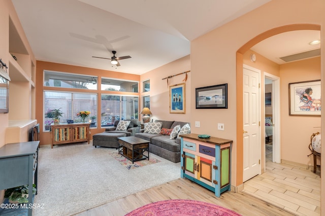 living area featuring baseboards, a ceiling fan, arched walkways, and light wood-style floors