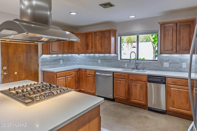 kitchen with appliances with stainless steel finishes, island exhaust hood, a sink, light countertops, and tasteful backsplash