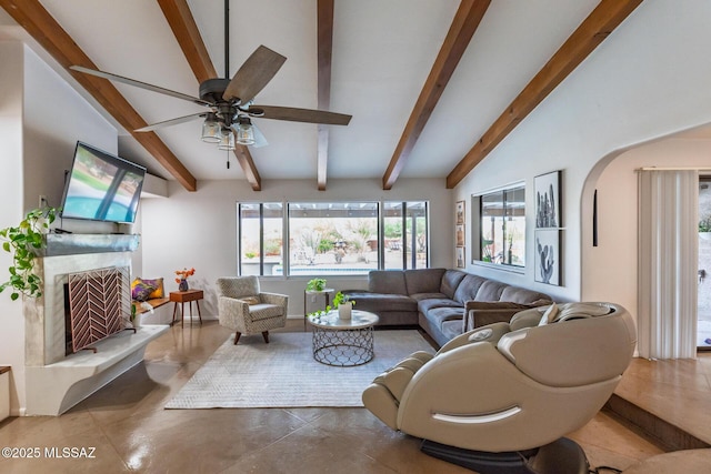 living area with beamed ceiling, ceiling fan, arched walkways, a fireplace, and finished concrete flooring