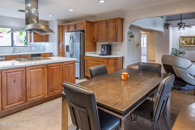 kitchen with appliances with stainless steel finishes, arched walkways, light countertops, brown cabinets, and tasteful backsplash
