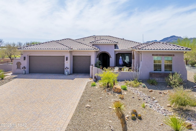mediterranean / spanish house featuring a tile roof, decorative driveway, a garage, and stucco siding