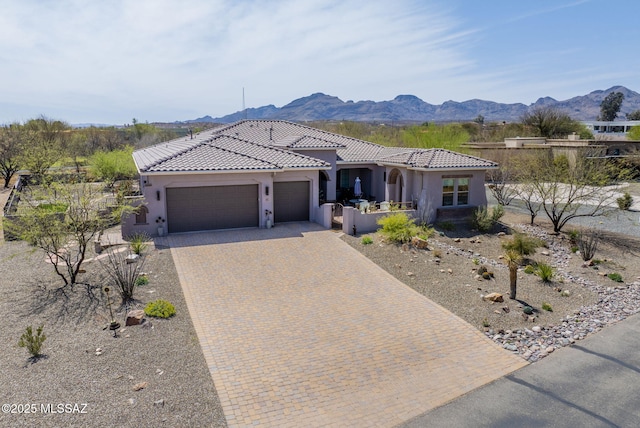 view of front of property with decorative driveway, an attached garage, a tile roof, stucco siding, and a mountain view