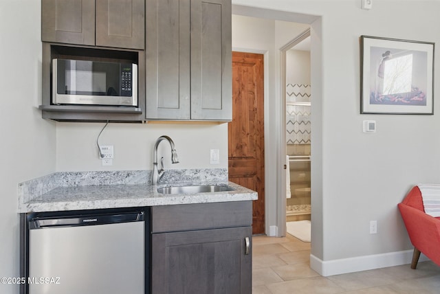 kitchen with light stone counters, a sink, dishwashing machine, stainless steel microwave, and baseboards