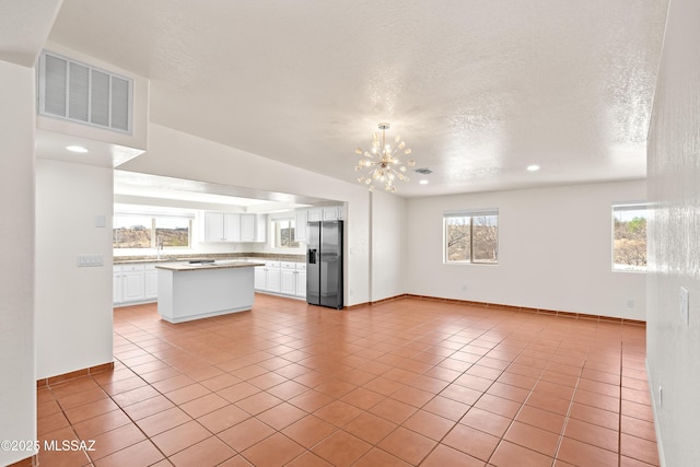kitchen with light tile patterned floors, visible vents, white cabinetry, stainless steel refrigerator with ice dispenser, and a notable chandelier