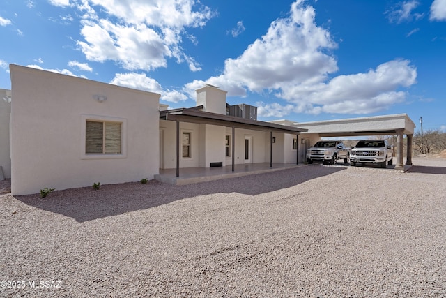 back of property with stucco siding, gravel driveway, and a carport