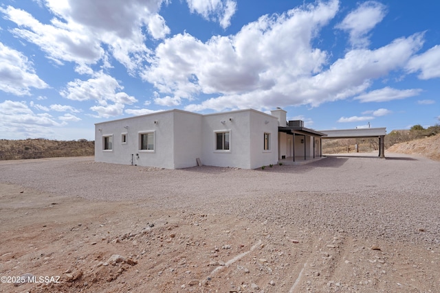 back of house with gravel driveway and stucco siding