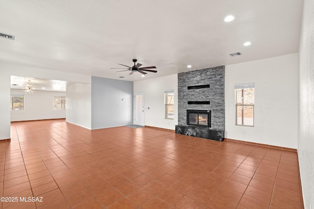 unfurnished living room with a stone fireplace, a wealth of natural light, visible vents, and tile patterned flooring