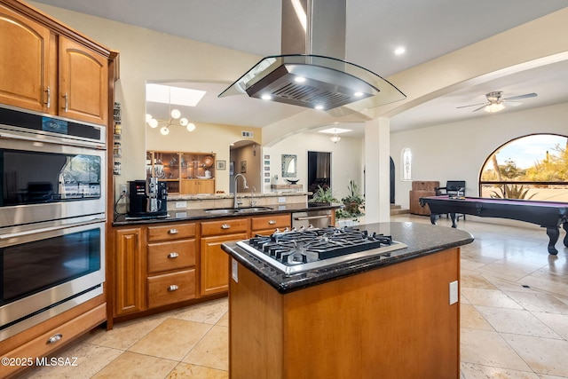 kitchen featuring appliances with stainless steel finishes, a sink, arched walkways, open floor plan, and island range hood