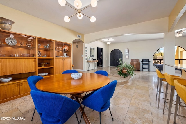 dining area with stone tile floors, arched walkways, an inviting chandelier, and visible vents
