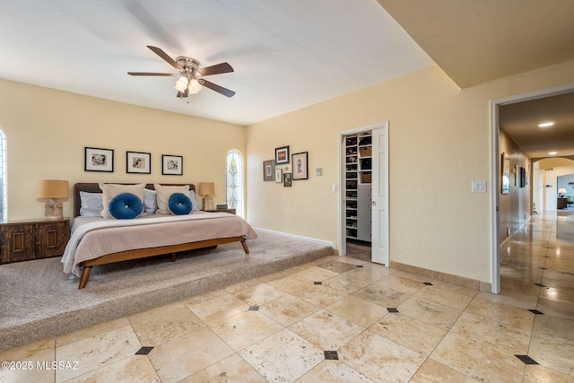 bedroom featuring a walk in closet, a ceiling fan, arched walkways, baseboards, and light tile patterned flooring