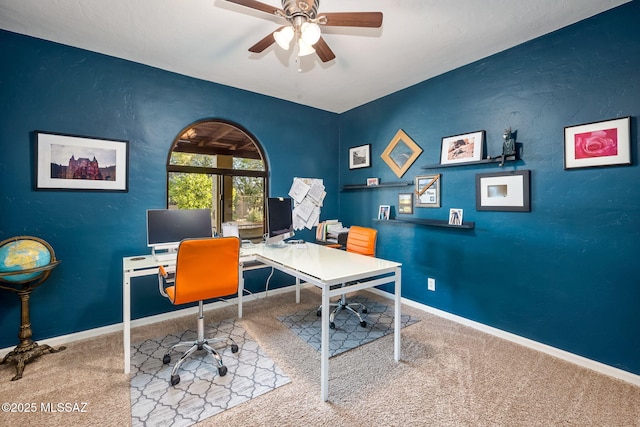 carpeted office featuring baseboards, a textured wall, and a ceiling fan
