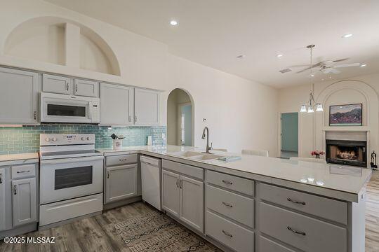 kitchen with light countertops, a peninsula, gray cabinetry, and white appliances