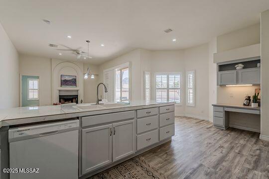 kitchen featuring gray cabinets, a sink, dishwasher, a fireplace, and wood finished floors