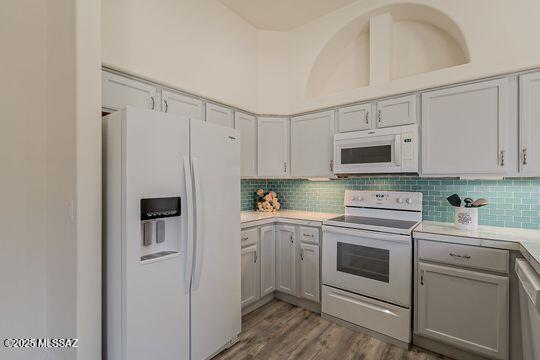 kitchen with light countertops, white appliances, wood finished floors, tasteful backsplash, and gray cabinetry