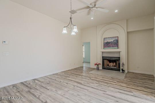 unfurnished living room featuring baseboards, wood finished floors, ceiling fan, and a large fireplace