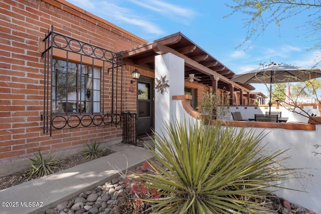 view of exterior entry with brick siding, ceiling fan, and area for grilling
