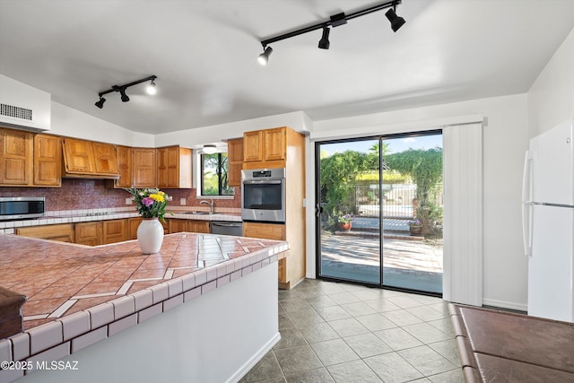 kitchen featuring stainless steel appliances, a sink, tasteful backsplash, tile counters, and rail lighting