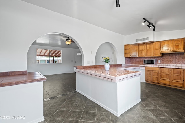 kitchen featuring backsplash, visible vents, tile countertops, stainless steel microwave, and ceiling fan