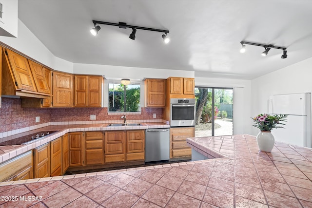 kitchen featuring track lighting, decorative backsplash, tile counters, and stainless steel appliances