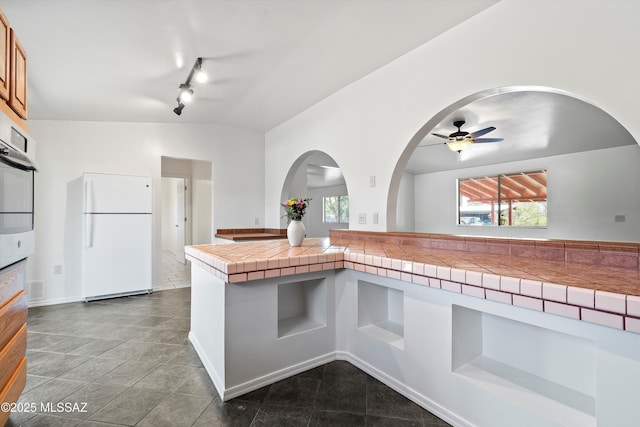 kitchen with tile counters, freestanding refrigerator, a healthy amount of sunlight, and a ceiling fan