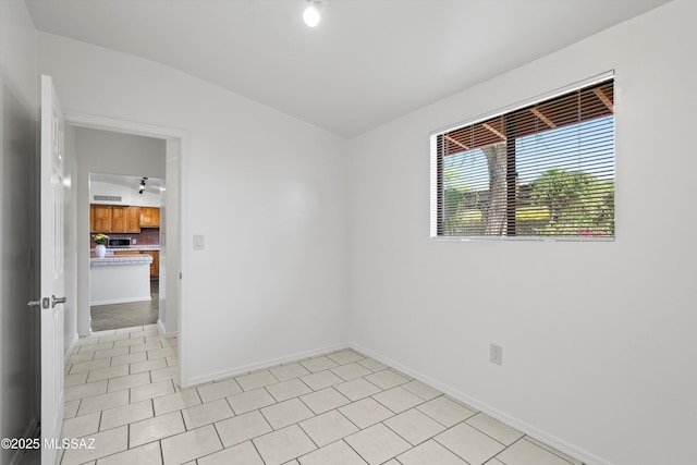spare room featuring track lighting and baseboards