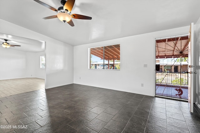 unfurnished room with stone tile floors, a ceiling fan, baseboards, and vaulted ceiling