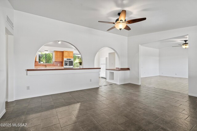 unfurnished living room featuring arched walkways, visible vents, a ceiling fan, and baseboards