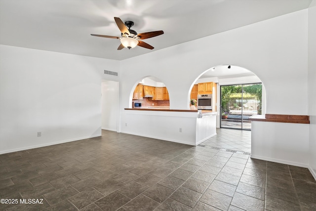 unfurnished living room featuring stone tile floors, ceiling fan, arched walkways, baseboards, and visible vents