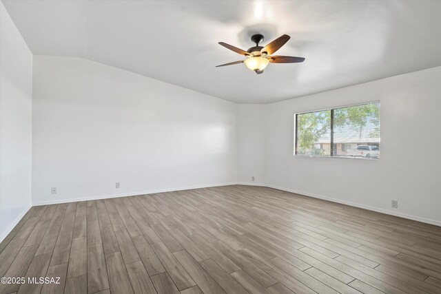 spare room with baseboards, vaulted ceiling, wood finished floors, and ceiling fan