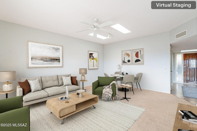 living area with a skylight, a ceiling fan, visible vents, and carpet