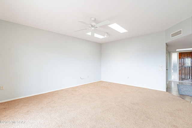 carpeted spare room featuring a ceiling fan, a skylight, and visible vents