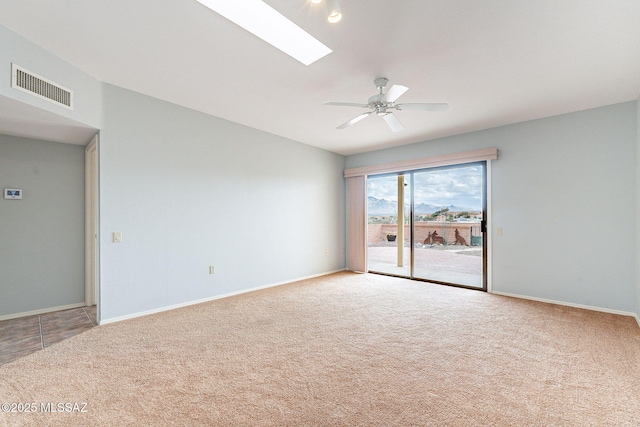 carpeted spare room featuring baseboards, visible vents, a skylight, and a ceiling fan