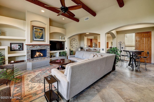 living room featuring a ceiling fan, arched walkways, beamed ceiling, a fireplace, and visible vents