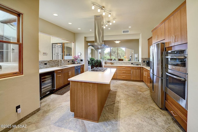 kitchen featuring island exhaust hood, wine cooler, light countertops, tasteful backsplash, and appliances with stainless steel finishes