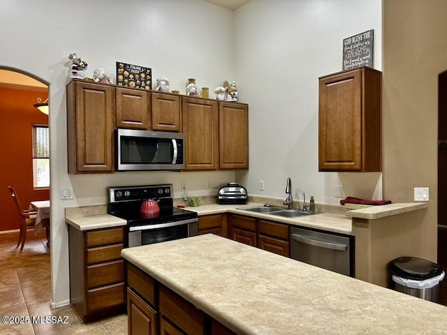 kitchen featuring arched walkways, a sink, light countertops, appliances with stainless steel finishes, and light tile patterned flooring