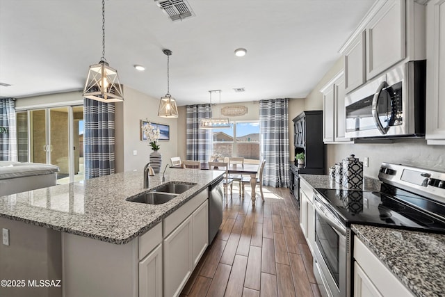 kitchen with a sink, appliances with stainless steel finishes, a center island with sink, dark wood-style flooring, and visible vents