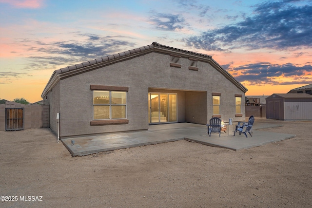 back of property with a storage unit, an outbuilding, a tiled roof, a patio area, and stucco siding