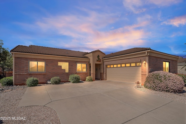 view of front of house featuring a tiled roof, an attached garage, brick siding, and concrete driveway