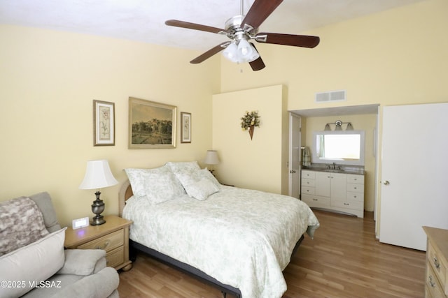 bedroom featuring visible vents, a sink, ceiling fan, vaulted ceiling, and wood finished floors