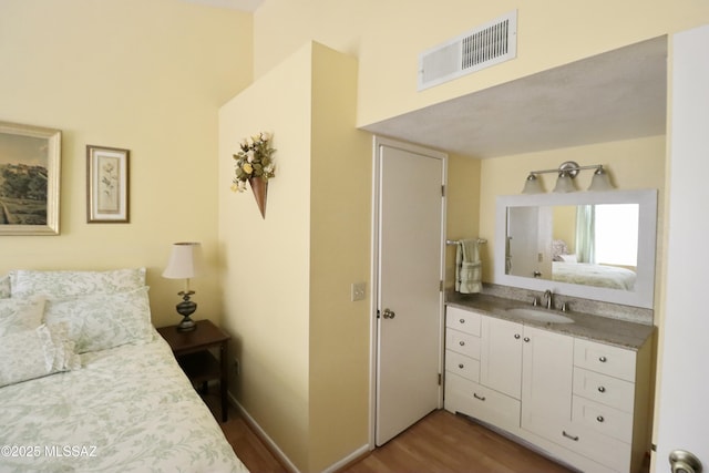 bedroom with baseboards, wood finished floors, a sink, and visible vents