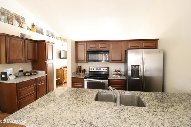 kitchen featuring stainless steel appliances, a sink, and light stone counters