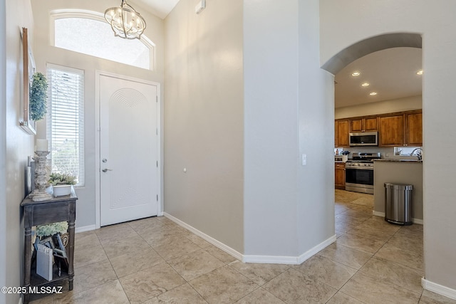 entrance foyer featuring light tile patterned flooring, baseboards, a high ceiling, a chandelier, and arched walkways