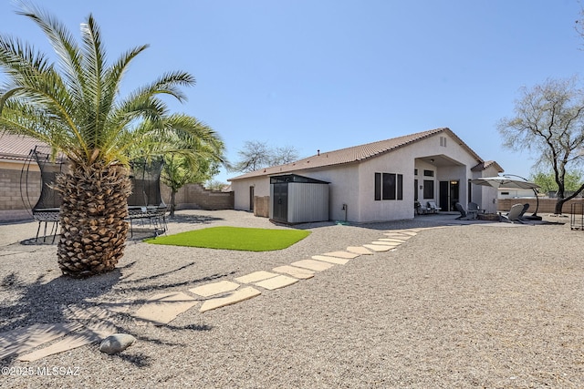 back of property with a patio, a fenced backyard, a trampoline, and stucco siding