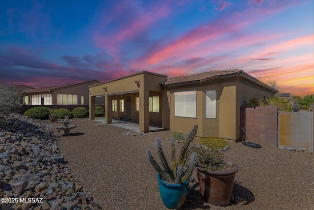 back of property at dusk featuring fence, a patio, and stucco siding