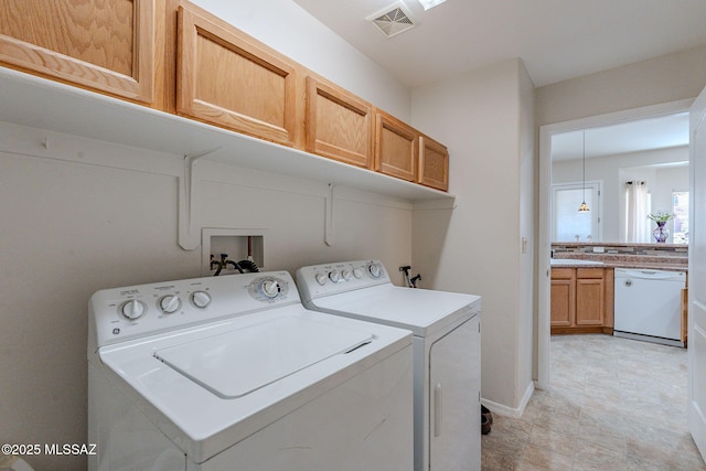 clothes washing area featuring separate washer and dryer, visible vents, baseboards, and cabinet space