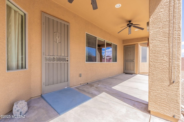 view of exterior entry featuring a patio, ceiling fan, and stucco siding
